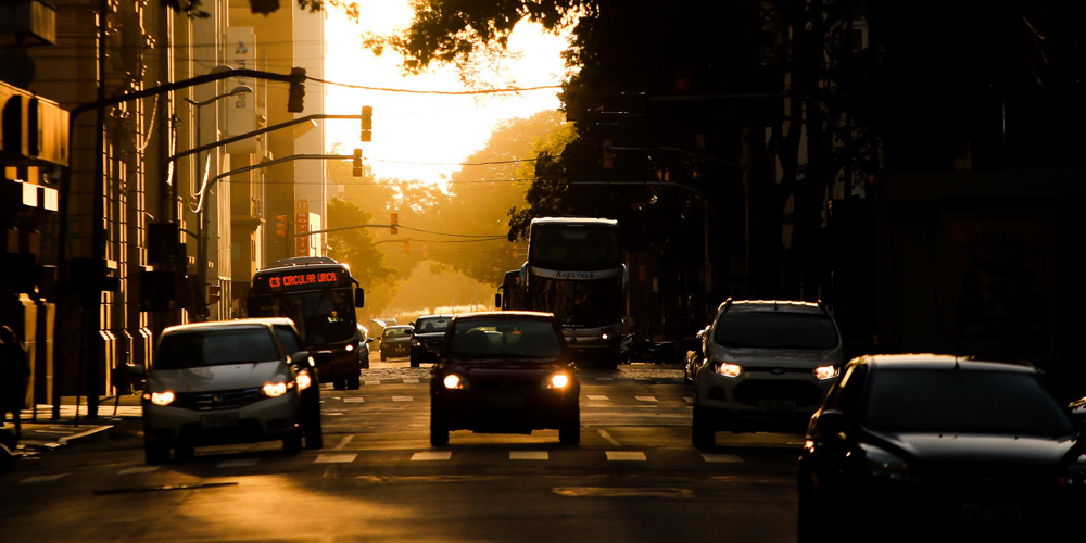 Carros e ônibus transitando pela cidade com sol ao fundo